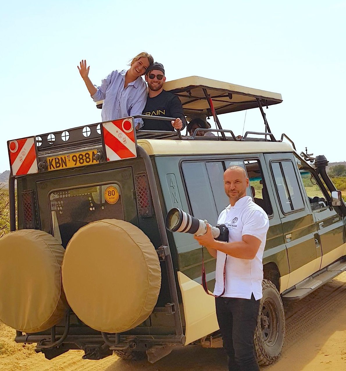 Real Masai Safari photographer with a long lens beside a safari vehicle, guests waving from the roof